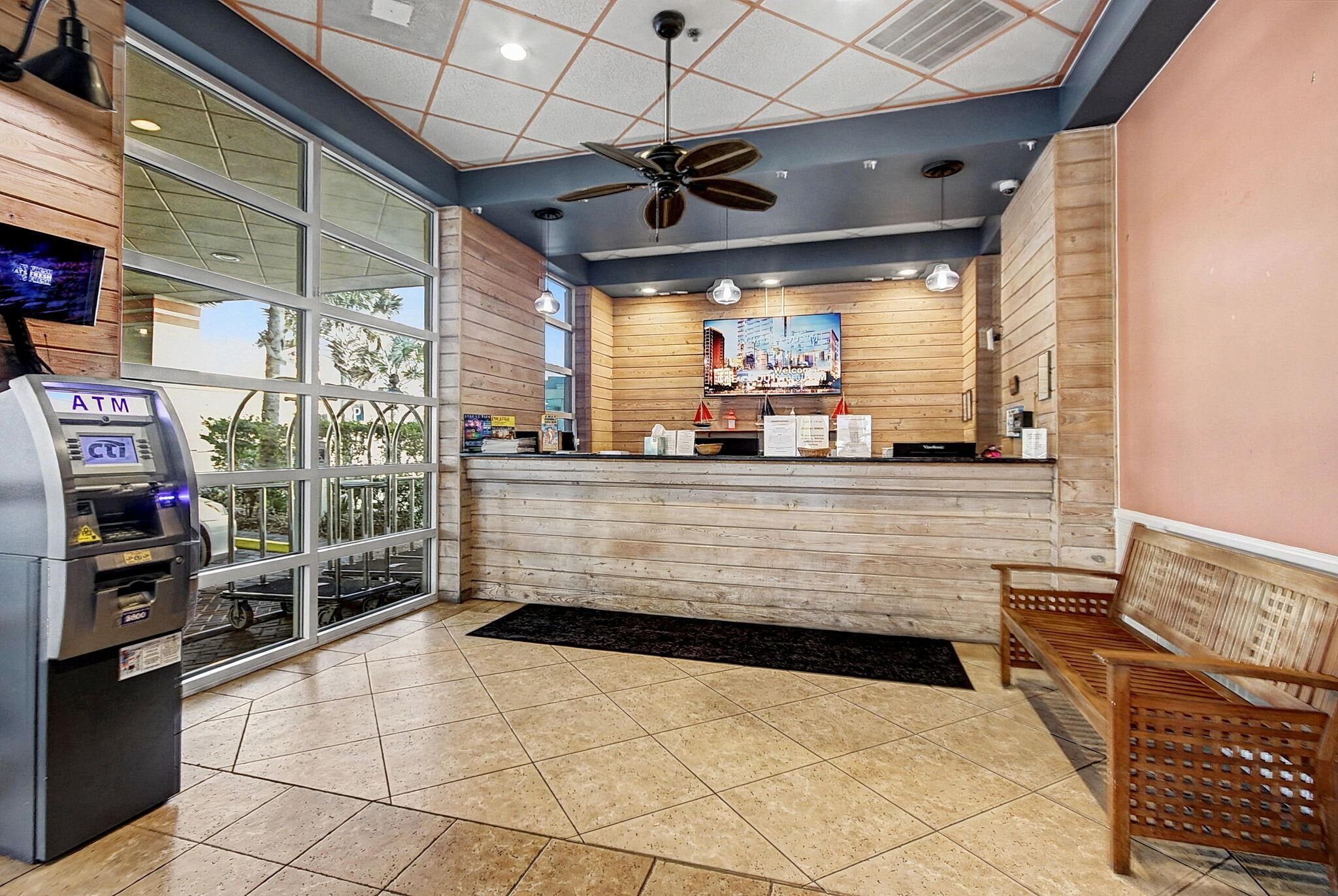 An indoor area with an ATM, wooden panel walls, a ceiling fan, and a bench.