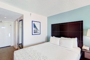 A hotel room with a large bed, a dark headboard, a framed picture on the wall, and a bedside telephone. - Cozy Oceanfront w/ Balcony & Breakfast + Pools (Myrtle Beach)