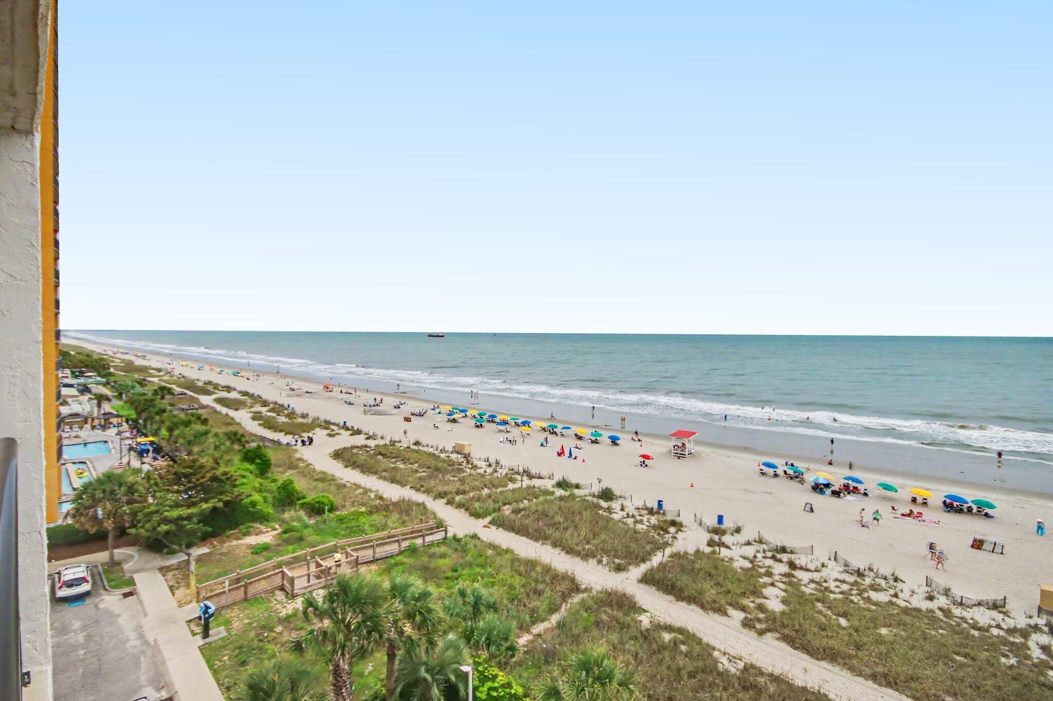 A beach with a wooden walkway, umbrellas, and a lifeguard tower.