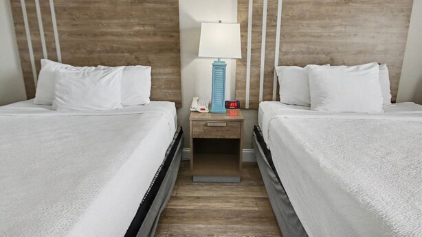 Habitació d'hotel amb dos llits, una tauleta de nit amb una làmpada i un rellotge digital.