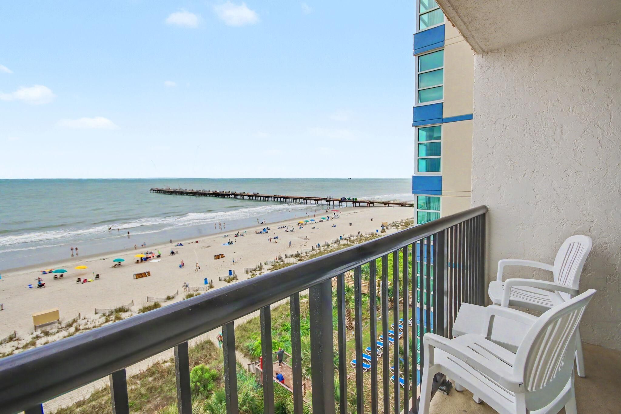 A balcony with a view of a beach, a pier, and a building with blue and white exterior.