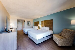 Ein Hotelzimmer mit zwei Betten, einem Schreibtisch mit Computer, einem Stuhl und einem hölzernen Kopfteil.