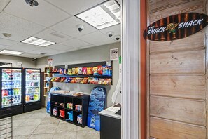 Un bar à collations avec des étagères remplies de produits, un congélateur et un comptoir sur lequel est affiché un panneau indiquant : « Le Snack Shack ».