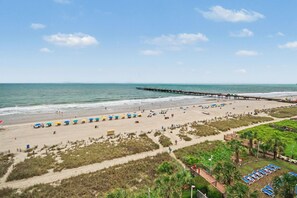 A beach with a pier extending into the ocean, sandy beach, and beach umbrellas. - Oceanfront Two Queen Standard Room + Lazy River & Hot Tub (Myrtle Beach)