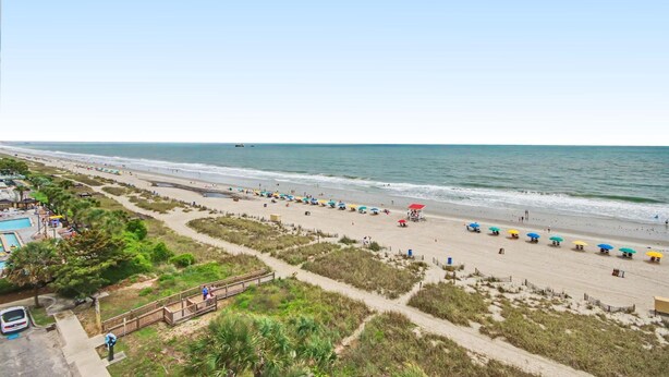 A beach with a lifeguard tower, umbrellas, and a clear view of the ocean. - Oceanfront Two Queen Standard Room + Lazy River & Hot Tub (Myrtle Beach)