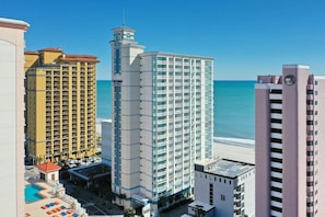 A high-rise hotel with multiple floors, a pool area, and a view of the beach. - Oceanfront Two Queen Standard Room + Lazy River & Hot Tub (Myrtle Beach)