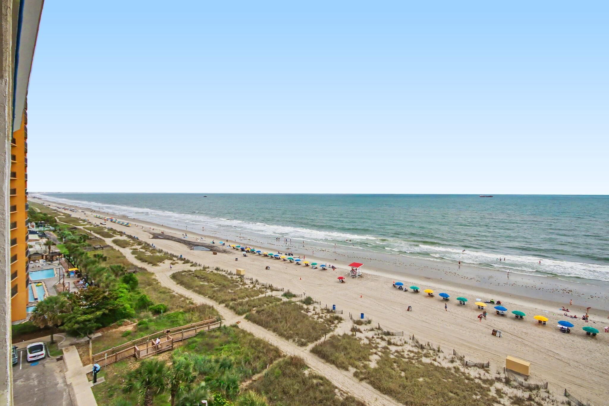 A beach with umbrellas and people, a clear sky, and a view of the ocean.