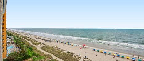 A beach with umbrellas and people, a clear sky, and a view of the ocean.