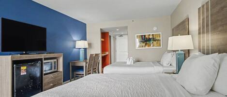 A hotel room with a bed, a TV, a desk with a lamp, and a microwave.