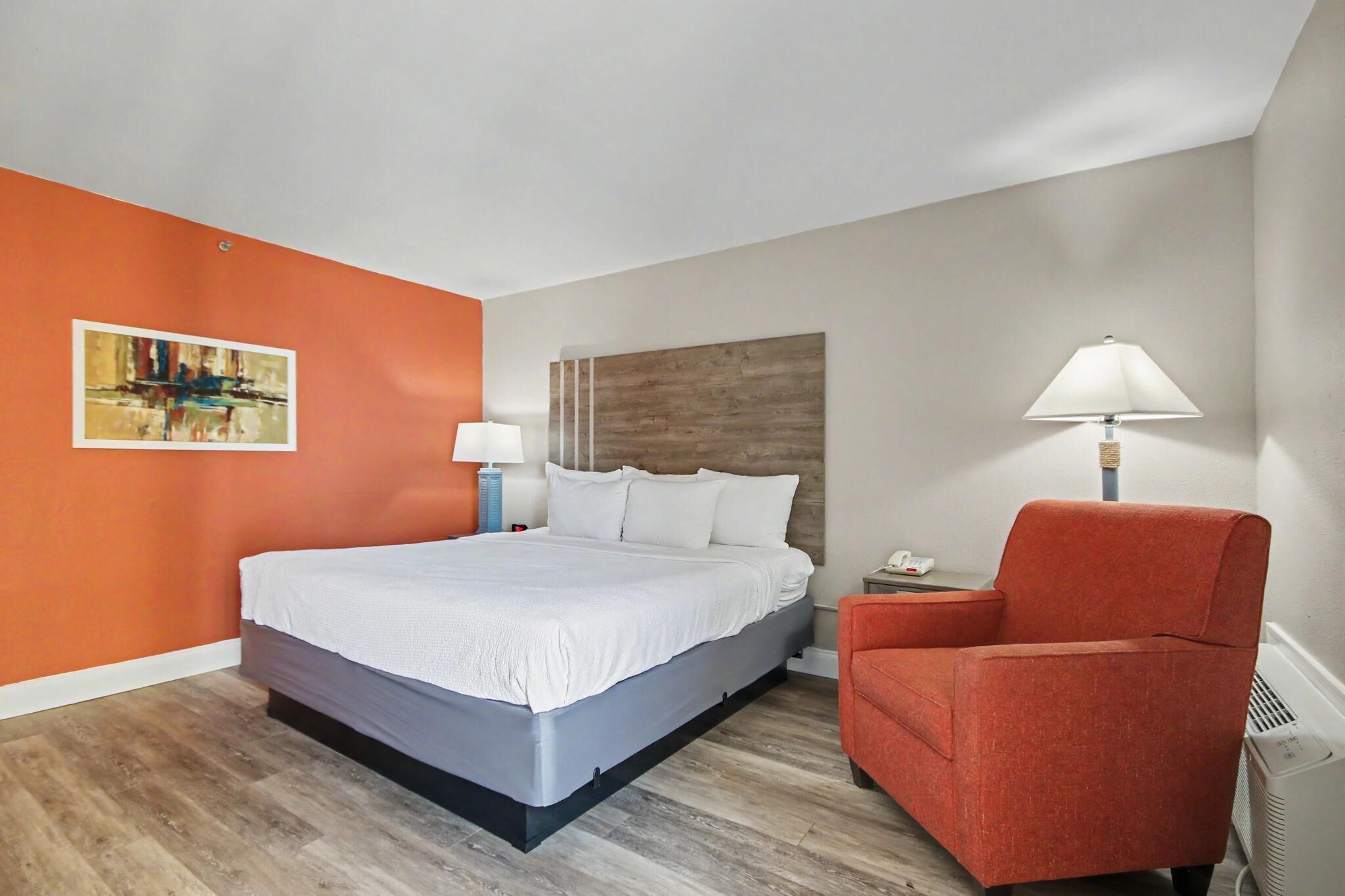 Ein Hotelzimmer mit Bett, Sessel, Nachttisch, Lampe und einem Bild an der Wand.
