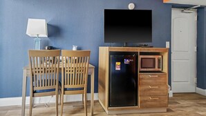 A room with a blue wall, a wooden table with chairs, a television, a refrigerator, and a microwave. - Resort View King Standard Room + Lazy River & Hot Tub (Myrtle Beach)