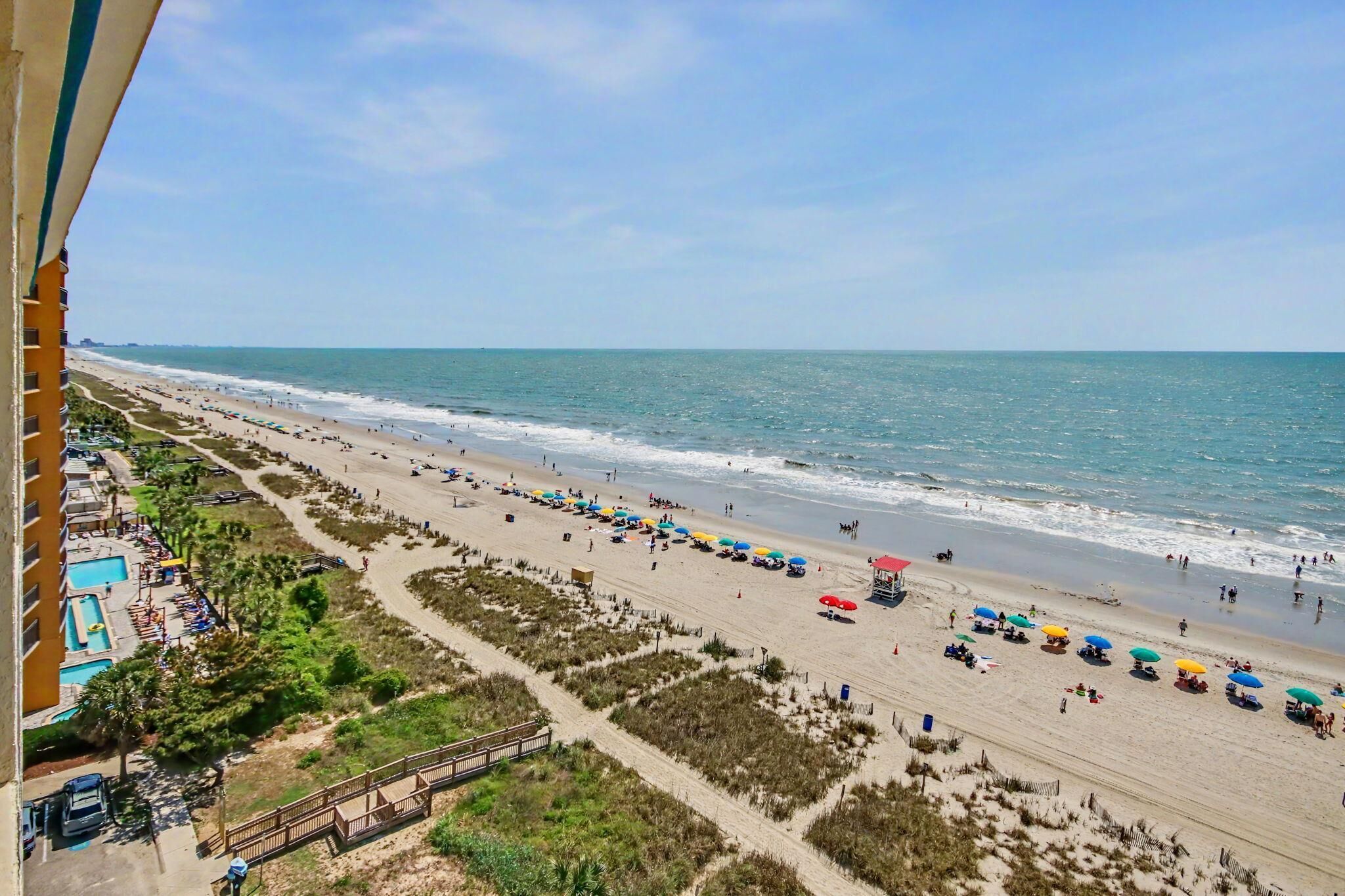 A beach with a long stretch of sand, a few umbrellas, and a clear view of the ocean.