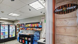 Eine kleine Imbissbar mit Regalen voller Snacks, einem Gefriertruhe und einer Theke, auf der ein Schild 'The Snack Shack' steht.