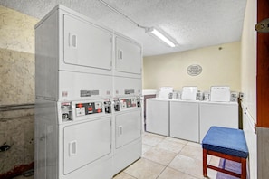 A laundry room with four stacked washers and dryers, a blue bench, and a wall sign indicating the room's purpose. - Oceanfront King Room + Lazy River & Hot Tub (Myrtle Beach)