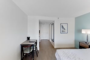 Ein Hotelzimmer mit einem Bett, einem Schreibtisch mit Stühlen, einer Lampe und einem gerahmten Bild an der Wand.