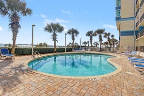 A pool area with lounge chairs, palm trees, and a view of the ocean. - Oceanfront Two Queen Room + Lazy River & Hot Tub (Myrtle Beach)