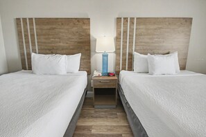 A hotel room with two beds, a nightstand with a lamp, and a small table. - Oceanfront Two Queen Room + Lazy River & Hot Tub (Myrtle Beach)