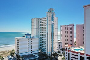 A multi-story hotel with a central tower, a swimming pool, and a beach view. - Oceanfront Two Queen Room + Lazy River & Hot Tub (Myrtle Beach)