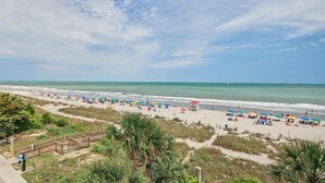 A beach with a wooden walkway, beach umbrellas, and a lifeguard tower. - Oceanfront Two Queen Room + Lazy River & Hot Tub (Myrtle Beach)