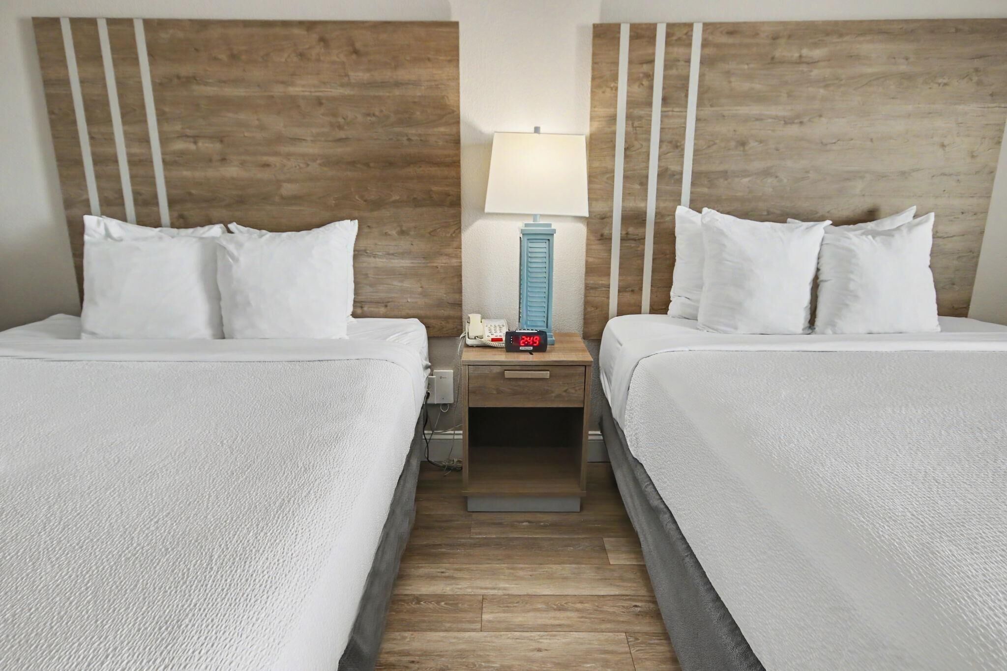A hotel room with two beds, a nightstand with a lamp, and a wooden headboard.