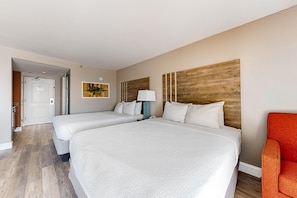 A hotel room with two beds, a wooden headboard, a painting, a lamp, and a red chair. - Cozy Oceanfront w/ Balcony & Breakfast + Pools (Myrtle Beach)