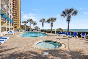 A pool area with lounge chairs, a hot tub, and palm trees. - Oceanfront Two Queen Room + Lazy River & Hot Tub (Myrtle Beach)