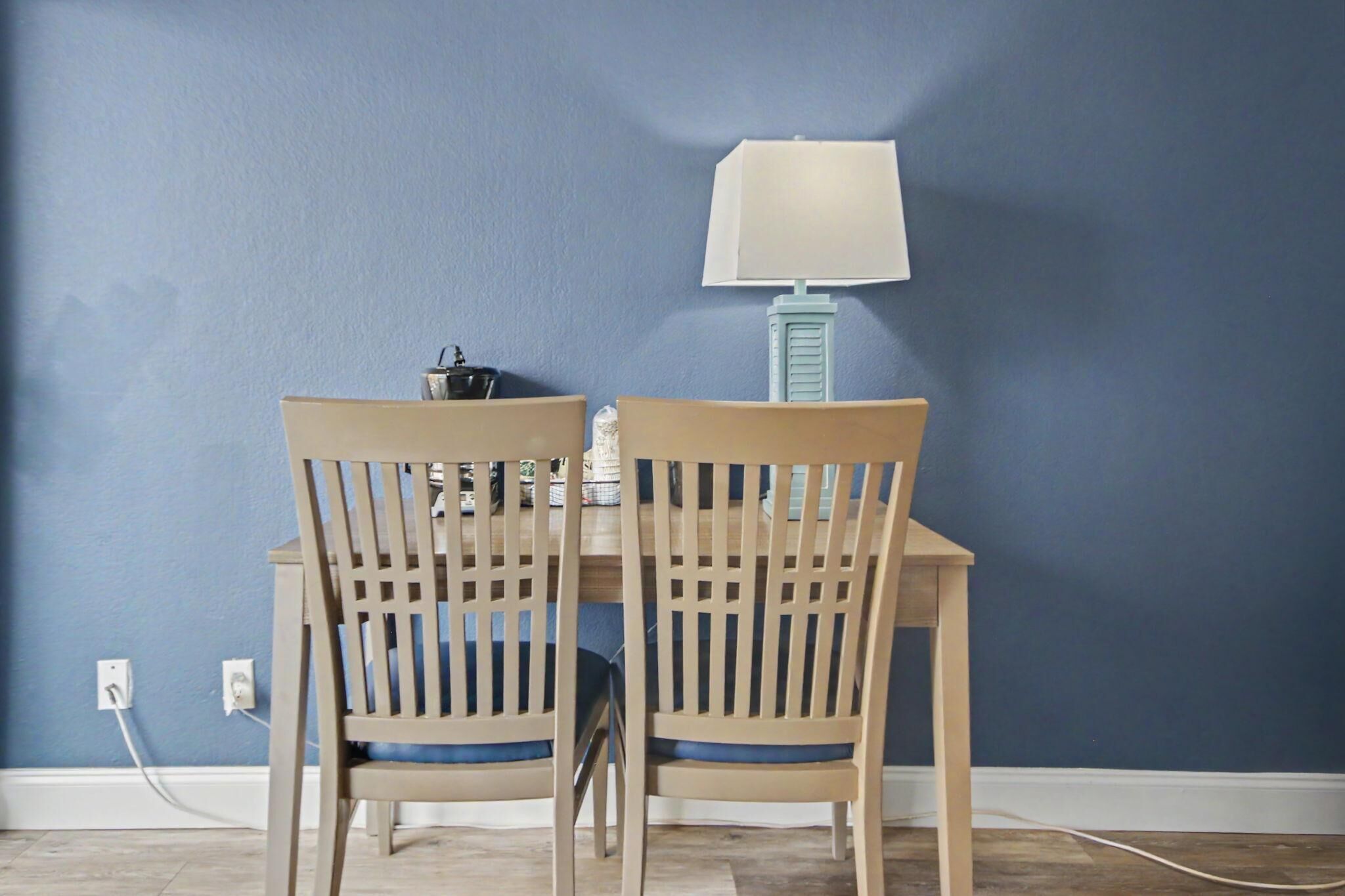 A dining area with two wooden chairs and a table, a lamp, and a wall socket.