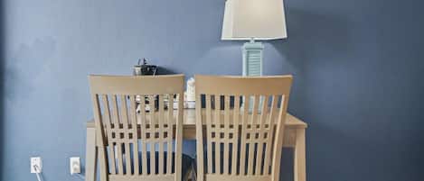 A dining area with two wooden chairs and a table, a lamp, and a wall socket.