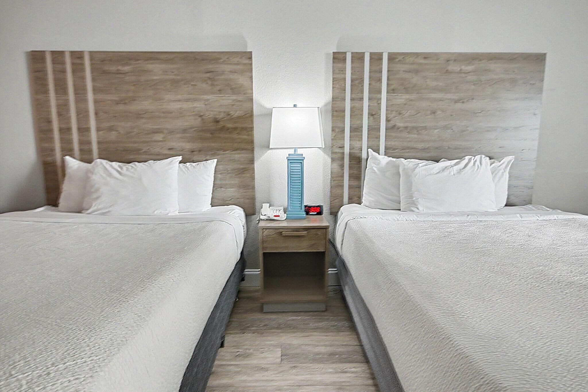 Una habitación de hotel con dos camas, una mesita de noche con lámpara, un reloj y un teléfono.