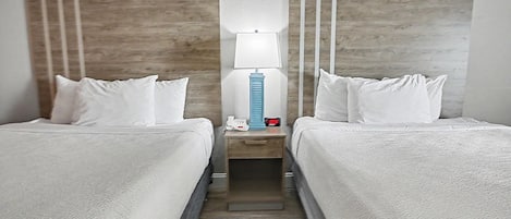 Una habitación de hotel con dos camas, una mesita de noche con lámpara, un reloj y un teléfono.