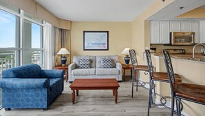 A living room with a sofa, coffee table, and dining area with chairs. - Oceanview 1BR Suite + Lazy River & Hot Tub (Myrtle Beach)