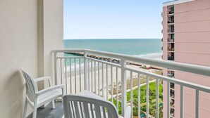 A balcony with white chairs, a view of the beach, and a pier. - Oceanview 1BR Suite + Lazy River & Hot Tub (Myrtle Beach)