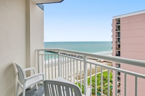 Ein Balkon mit weißen Stühlen, Blick auf den Strand und einen Steg.
