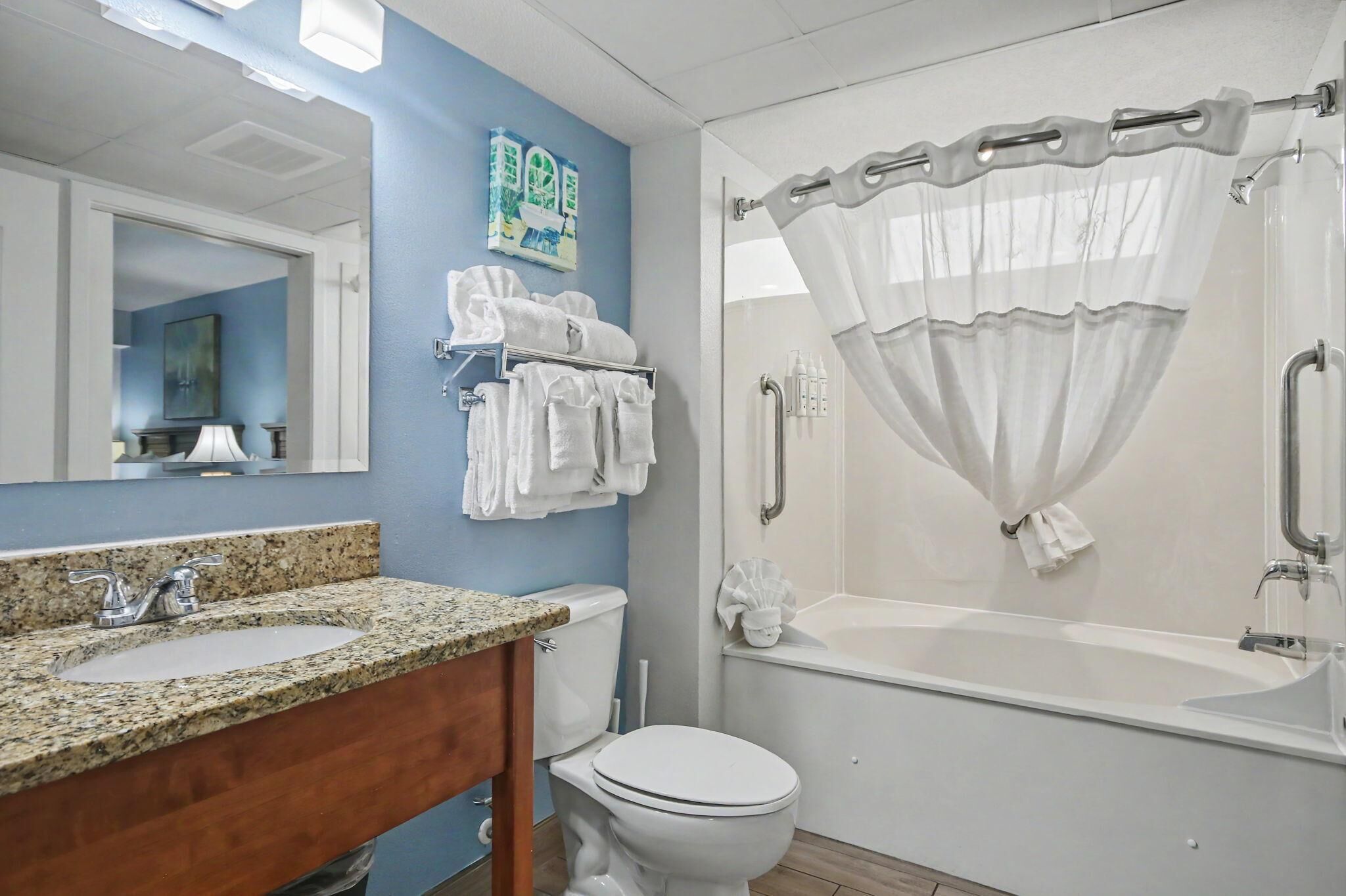 A bathroom with a granite countertop sink, white toilet, and a walk-in shower with a white curtain.
