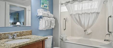 A bathroom with a granite countertop sink, white toilet, and a walk-in shower with a white curtain.