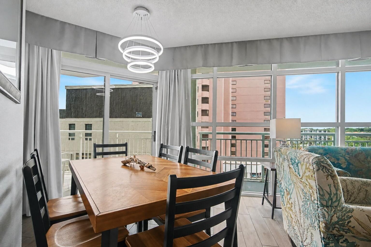 A modern hotel room with a dining area, a sofa, and large windows offering a city view.