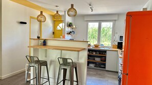 Une cuisine compacte dotée d’un plan de travail en bois, de deux tabourets de bar, de luminaires suspendus et d’une fenêtre donnant sur un espace verdoyant.