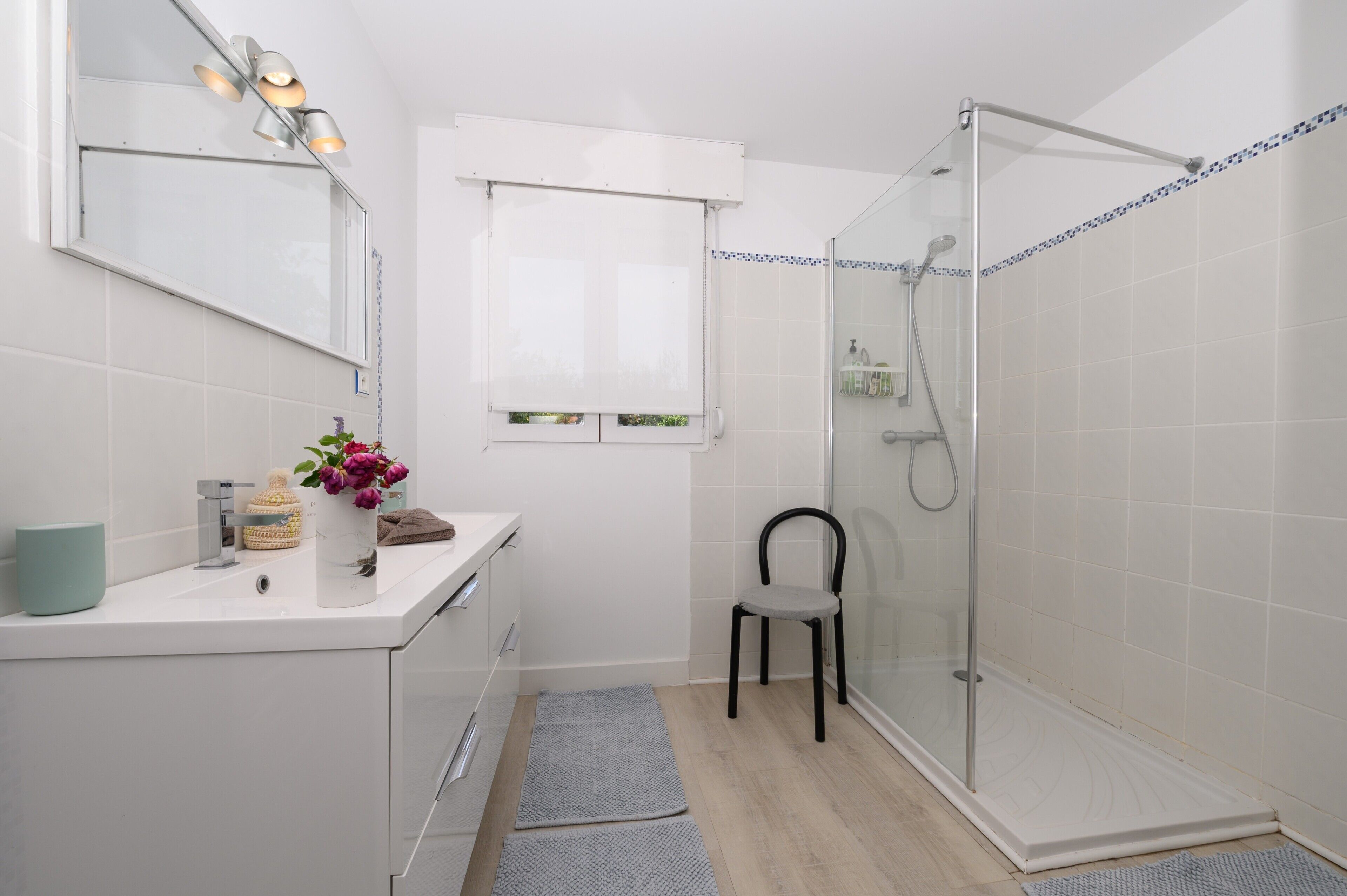 Une salle de bain moderne équipée d’une douche, d’un lavabo, d’un miroir et d’une chaise.