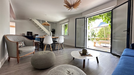 A modern living room with a sofa, ottoman, and dining area with chairs.. Maison Hoali – Presqu’île de Rhuys: Sea View, Wi-Fi, and Air Conditioning