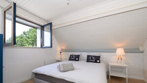 Ein Schlafzimmer mit einem großen Bett, einem Fenster, einem Nachttisch und einer Lampe.