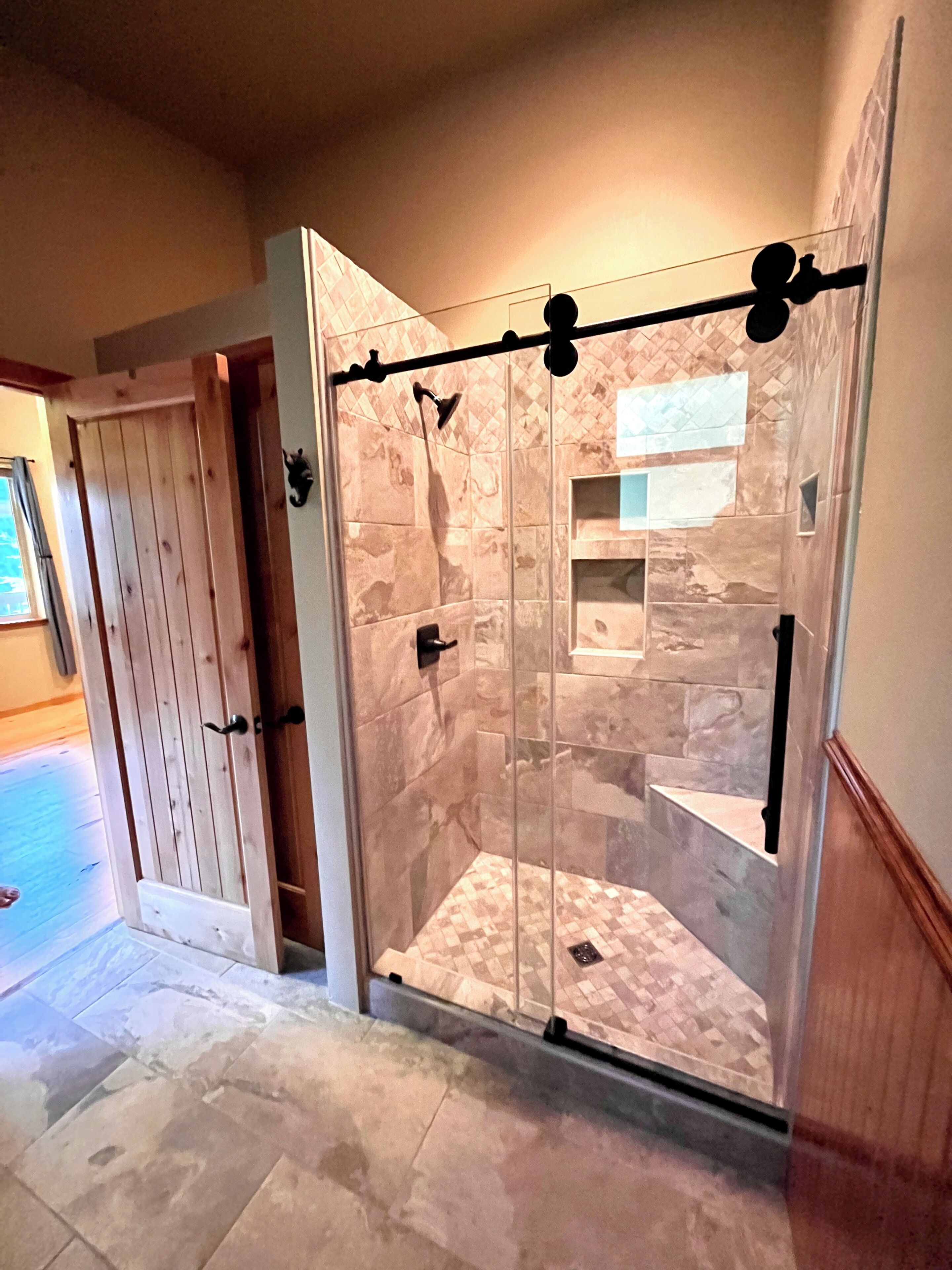 Un espace douche doté d’une porte en verre, d’une porte en bois et d’un sol carrelé.