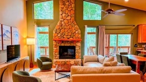 Una sala de estar con chimenea de piedra, un sofá, dos sillones, un televisor y un comedor con mesa y sillas.