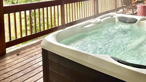 Un jacuzzi en una terraza de madera con vistas a árboles y montañas.