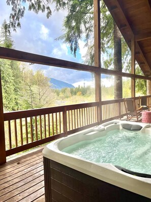 Un bain à remous sur une terrasse en bois, avec vue sur les arbres et les montagnes.