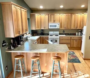 Una cocina con armarios de madera, una isla central con taburetes, microondas, estufa y refrigerador.