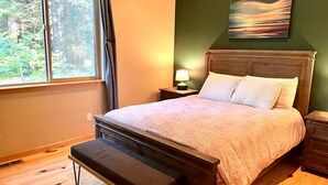 Un dormitorio con cama, banco, mesita de noche, lámpara y un cuadro en la pared.