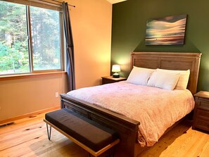 Un dormitorio con cama, banco, mesita de noche, lámpara y un cuadro en la pared.