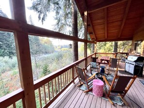 Une terrasse en bois offrant une vue sur une forêt, avec des sièges d’extérieur et un barbecue.