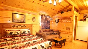 A log cabin interior with a bed, sofa, and dining table. - Bears Den, studio cabin, full kitchen, cover carport, Restmore Inn, Hill City (Hill City)