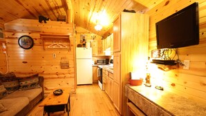 A cabin interior with a wooden interior, a television mounted on the wall, a kitchen area, and a sofa. - Bears Den, studio cabin, full kitchen, cover carport, Restmore Inn, Hill City (Hill City)